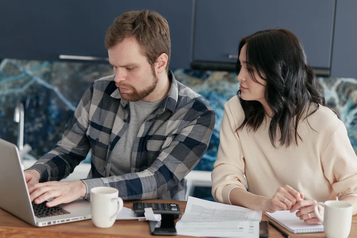 Par som planerar bröllopsbudget med checklista och laptop vid köksbordet